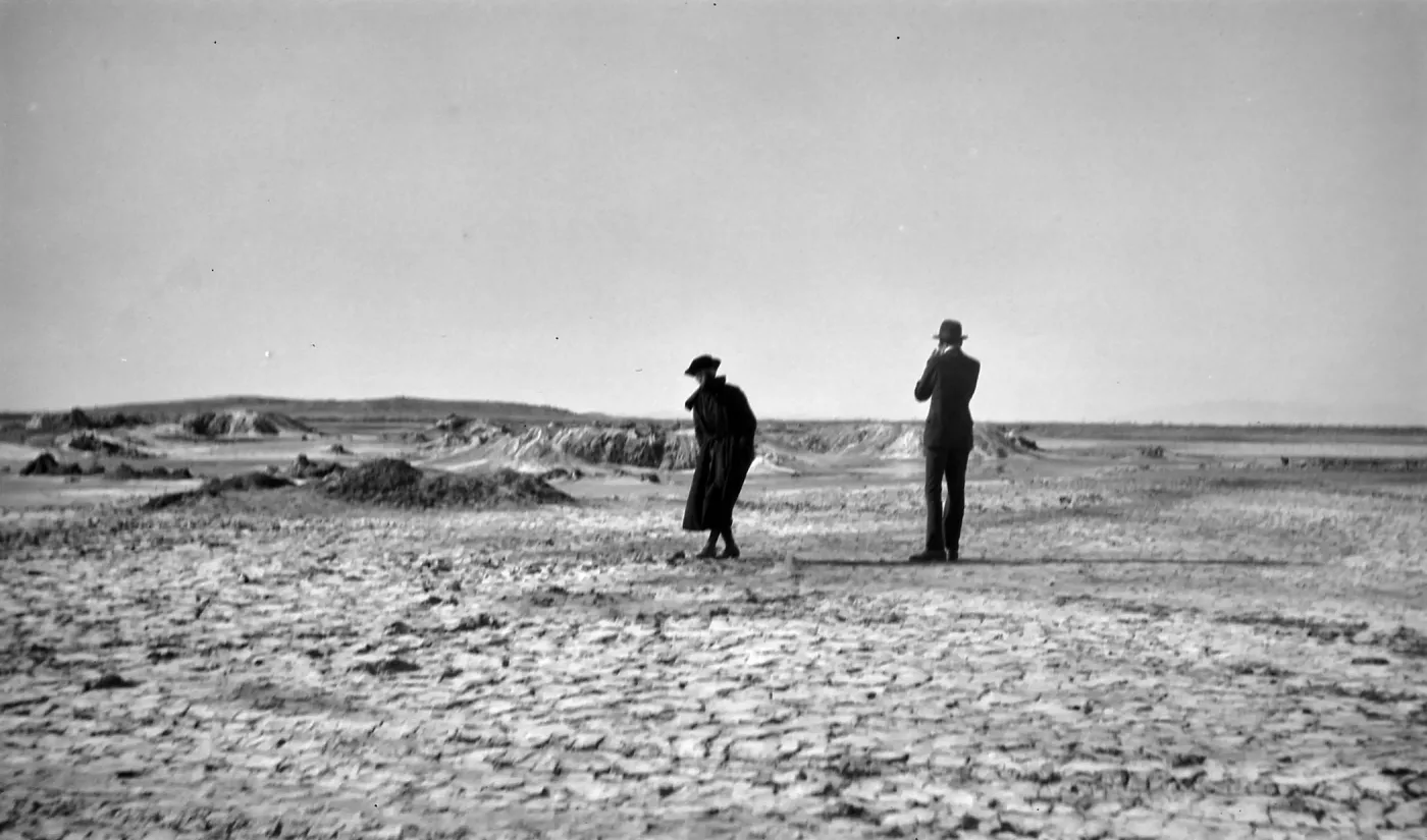 Black and white photograph of a man and woman standing on a dried-up mud flat that extends far into the distance.