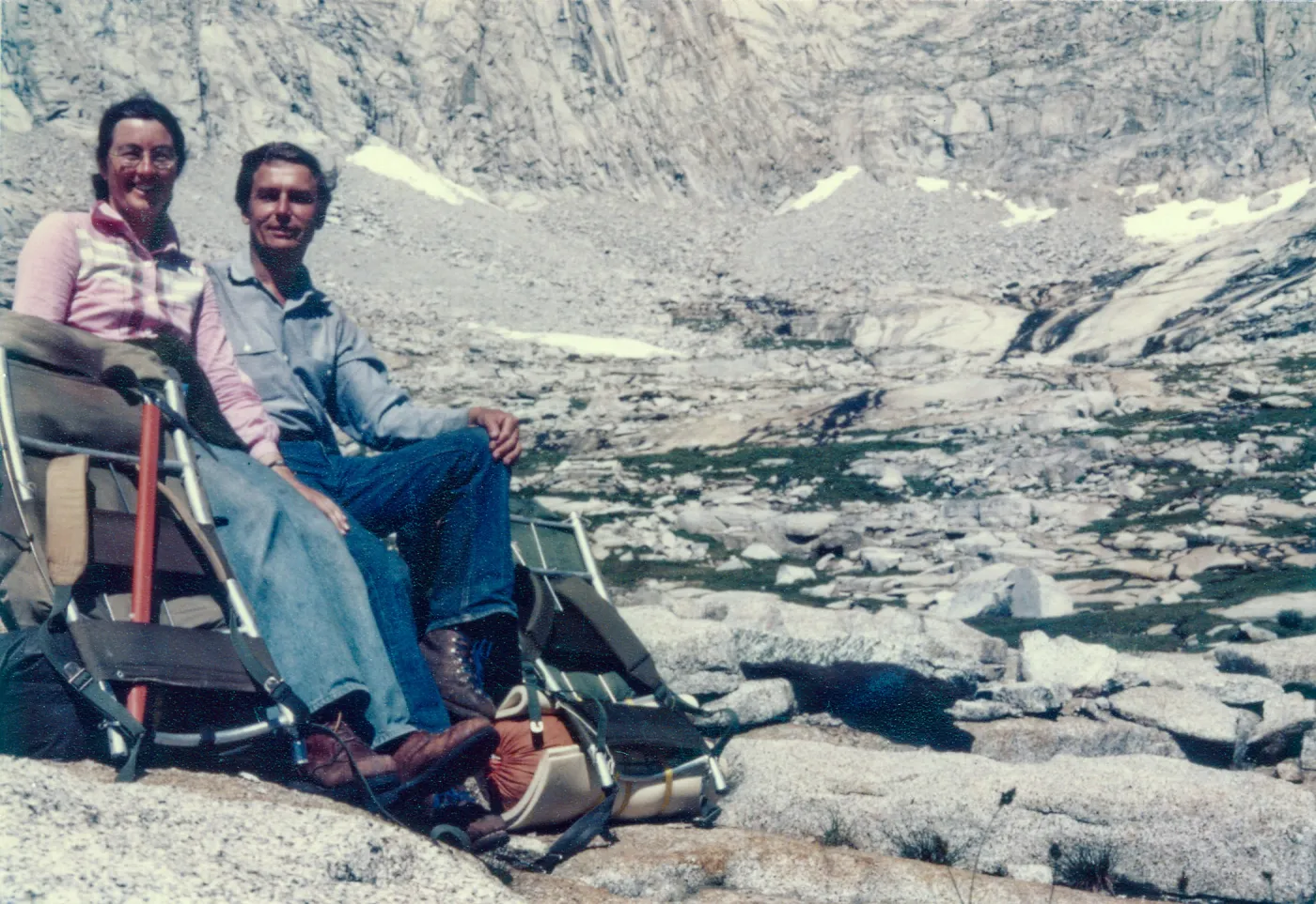 Photo of male and female explorers with camping gear in bald and snowy mountains with rocky terrain. 