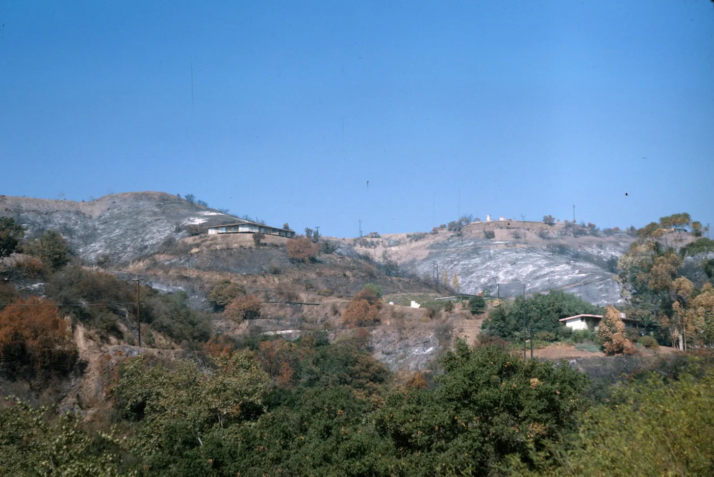 A few low, white houses on rounded mountain slopes among brown, burned vegetation.