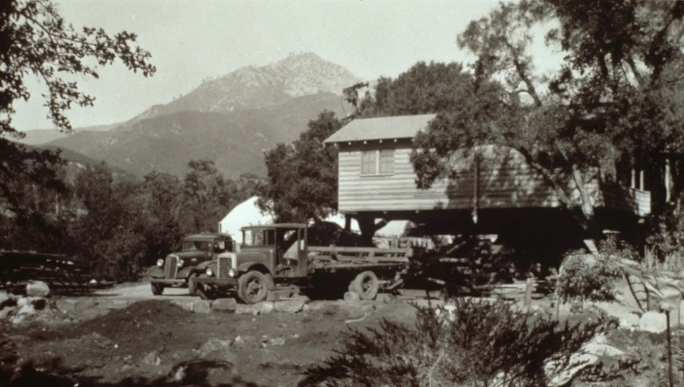 duplicate of SBBG_PR_02742, Moving the Cottage building, with greenhouse in background