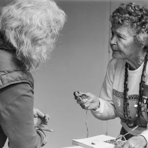 a black and white photo of an older woman with white hair and their back facing the camera talking to an older woman sharing an activity.