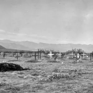 Black and white photograph of a graveyard with black and white crosses with hills in the distance.