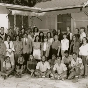 A black and white photo of 34 people posed in the corner of a stone patio in front of a one-story building. Eight people sit or kneel on the ground and the rest are arranged in two rows behind them.