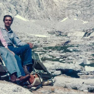 Photo of male and female explorers with camping gear in bald and snowy mountains with rocky terrain. 