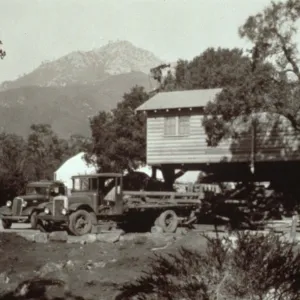 duplicate of SBBG_PR_02742, Moving the Cottage building, with greenhouse in background